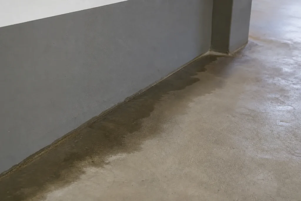 Piso de garagem residencial apresenta área localizada de umidade próxima à parede.