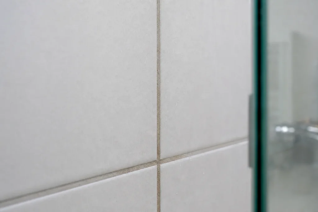 Rejunte escurecido entre azulejos claros de box de banheiro.