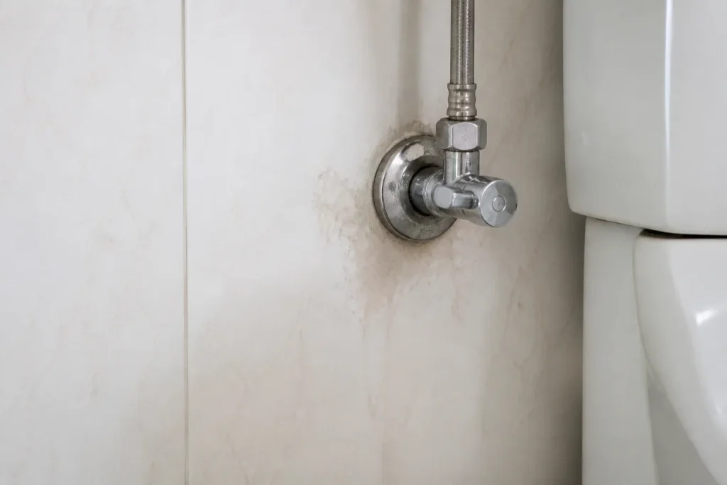 Registro hidráulico em parede residencial apresenta sinal discreto de umidade.