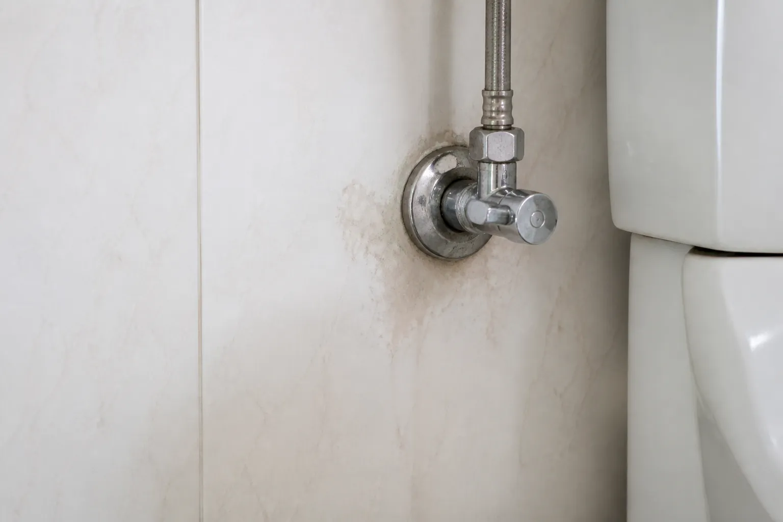 Registro hidráulico em parede residencial apresenta sinal discreto de umidade.