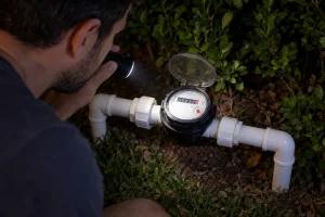 Morador confere hidrômetro à noite para investigar consumo contínuo de água.